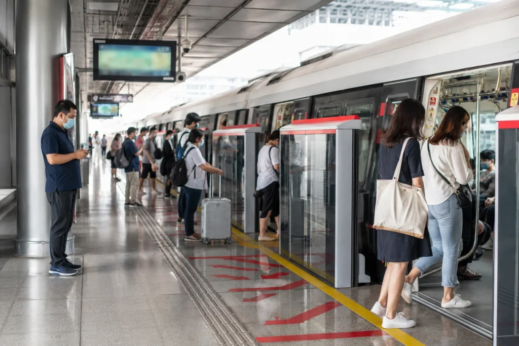 Commuters and tourists using a modern Singapore MRT station with EZ-Link cards, luggage, digital signs, and clean train platforms.

